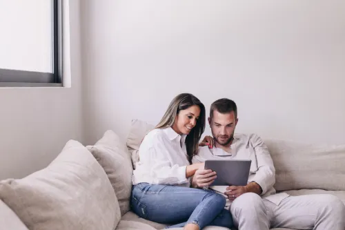 Casal sentado no sofá a consultar um tablet em conjunto